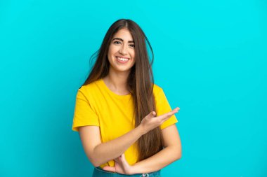 Mavi arka planda izole edilmiş genç beyaz kadın bir fikir sunuyor ve gülümsüyor.