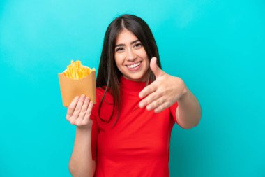 Genç beyaz kadın patates kızartması yakalıyor. Mavi arka planda izole edilmiş, iyi bir anlaşma için el sıkışıyor.