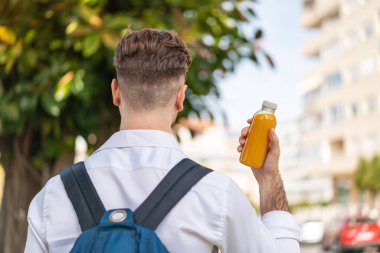 Genç yakışıklı adam arka tarafta portakal suyu tutuyor.