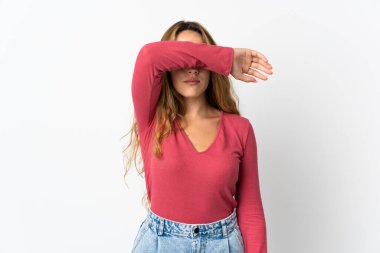 Mavi arka planda izole edilmiş genç sarışın kadın gözlerini elleriyle kapatıyor.