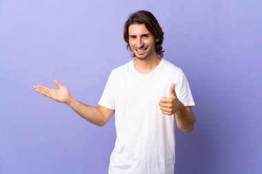 Mor arka planda izole edilmiş genç bir adam. Kopyalama alanı hayali olarak avucunun içinde duruyor. Bir ilan vermek ve onaylamak için.