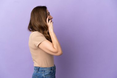 Orta yaşlı beyaz kadın cep telefonu kullanıyor. Mor arka planda izole edilmiş. Yan pozisyonda gülüyor.