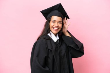 Pembe arka planda izole edilmiş genç Kolombiyalı kadın elini kulağına koyarak bir şeyler dinliyor.