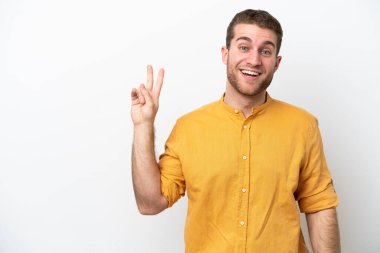 Beyaz arka planda izole edilmiş genç beyaz adam gülümsüyor ve zafer işareti gösteriyor.