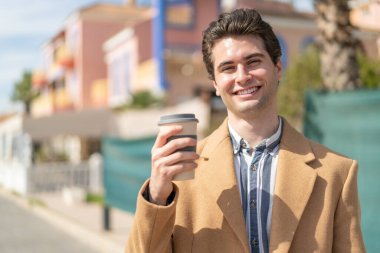 Genç yakışıklı bir adam elinde kahveyle mutlu bir ifadeyle.