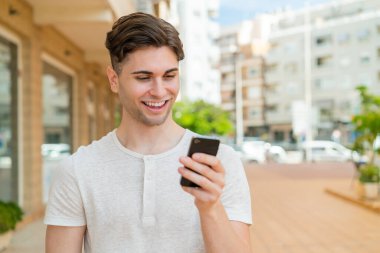 Genç yakışıklı adam cep telefonuyla mesaj ya da e-posta yolluyor.