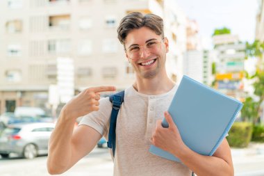 Genç yakışıklı bir öğrenci açık havada ve onu işaret ediyor.