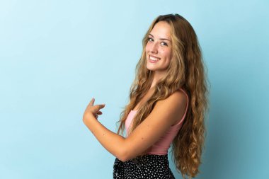 Mavi arka planda izole edilmiş genç sarışın kadın geriye işaret ediyor
