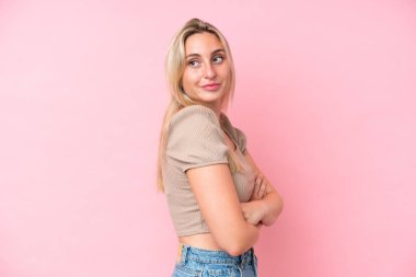 Pembe arka planda soyutlanmış genç beyaz kadın yana bakıyor ve gülümsüyor.