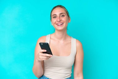 Genç beyaz kadın mavi arka planda cep telefonu kullanıyor.