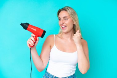 Mavi arka planda saç kurutma makinesi tutan beyaz bir kadın zaferi kutluyor.