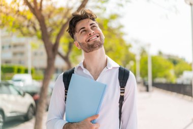 Genç ve yakışıklı bir öğrenci gülümserken yukarı bakıyor.