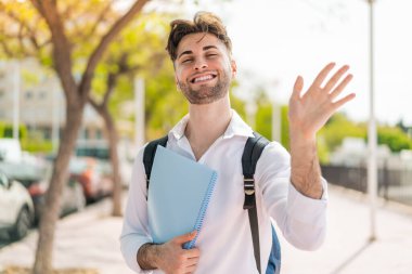 Genç ve yakışıklı bir öğrenci, elinde mutlu bir ifadeyle selamlıyor.