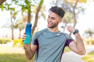 Genç yakışıklı sporcu dışarıda bir şişe suyla zaferi kutluyor.
