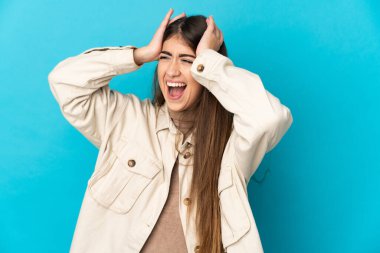 Genç beyaz kadın, mavi arka planda izole edilmiş ve intihar jesti yapmada sorun yaşıyor.