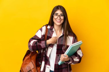 Sarı arka planda yalıtılmış genç bir bayan öğrenci. Sürpriz bir yüz ifadesi var.