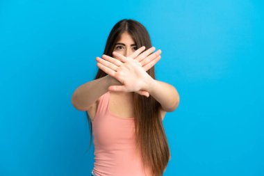 Kafkasyalı genç bir kadın, mavi arka planda izole edilmiş bir şekilde bir eylemi durdurmak için el hareketi yapıyor.