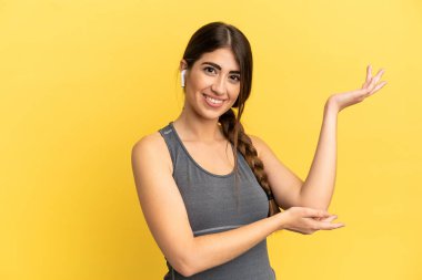 Sarı arka planda izole edilmiş beyaz kadın, davet edilmek için ellerini yana uzatıyor.