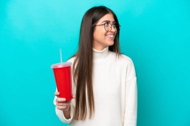 Mavi arka planda izole edilmiş soda içen beyaz bir kadın.