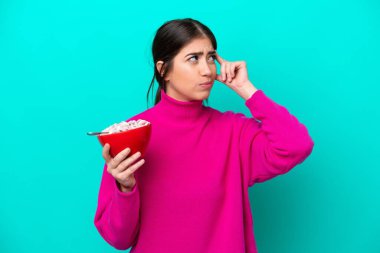 Beyaz bir kadın elinde bir kase mısır gevreği tutarken mavi arka planda kuşkuları ve şaşkın bir ifadeyle