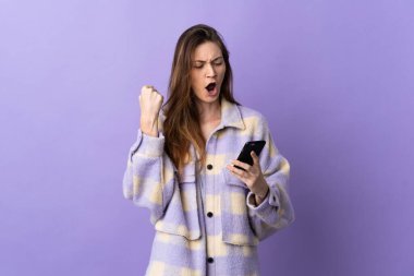 Genç İrlandalı kadın mor arka planda cep telefonu kullanarak ve zafer jesti yaparak izole edildi.