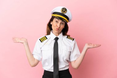 Orta yaşlı uçak pilotu kadın pembe arka planda izole edildi. El kaldırırken şüpheleri vardı.