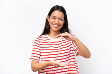 Beyaz arka planda izole edilmiş genç Kolombiyalı kadın bir ilan vermek için avucunun içinde hayali bir şey tutuyor.