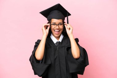 Young university Colombian woman graduate isolated on pink background with glasses and surprised