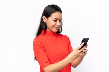 Beyaz arka planda izole edilmiş genç Kolombiyalı kadın cep telefonuyla mesaj ya da e-posta gönderiyor.