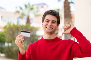 Dışarıda kredi kartı tutan genç yakışıklı adam gururlu ve kendini beğenmiş.
