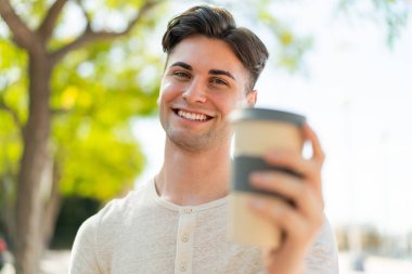 Genç yakışıklı bir adam elinde kahveyle mutlu bir ifadeyle.