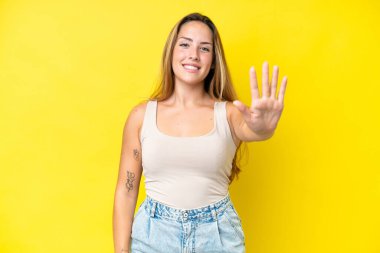 Sarı arka planda izole edilmiş genç beyaz kadın parmaklarıyla beşi sayıyor.