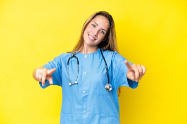 Sarı arka planda izole edilmiş genç cerrah kadın gülümseyerek seni işaret ediyor.