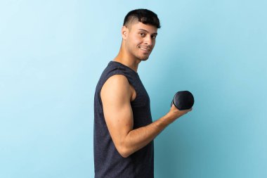 Mavi arka planda izole genç Kolombiyalı adam halter yapıyor.