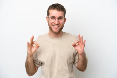 Beyaz arka planda izole edilmiş genç beyaz bir adam iki eliyle tamam işareti gösteriyor.