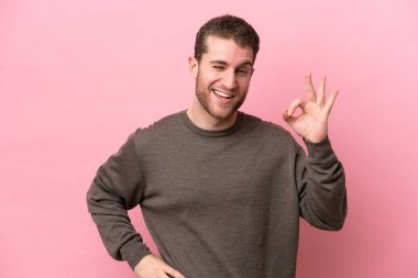 Pembe arka planda izole edilmiş genç beyaz adam parmaklarıyla tamam işareti gösteriyor.