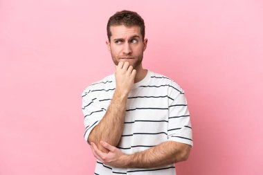 Pembe arka planda soyutlanmış genç beyaz bir adamın şüpheleri ve düşünceleri var.