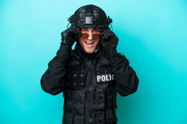 SWAT caucasian man isolated on blue background with glasses and surprised