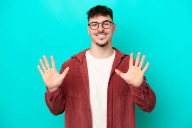 Mavi arka planda izole edilmiş beyaz tenli yakışıklı adam parmaklarıyla 10 'a kadar sayıyor.