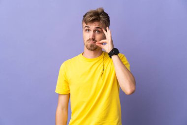 Mor arka planda izole edilmiş genç, yakışıklı sarışın adam sessizlik işareti gösteriyor.