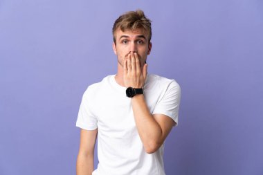 Mor arka planda izole edilmiş genç, sarışın bir adam. Ağzını eliyle kapatıyor.