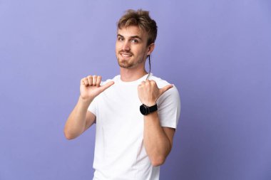 Mor arka planda izole edilmiş yakışıklı sarışın bir adam bir ürün sunmak için kenarı işaret ediyor.