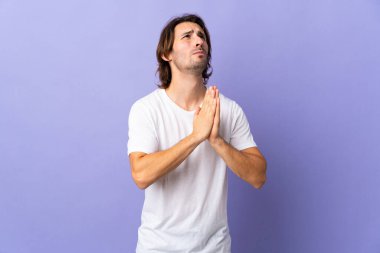 Mor arka planda izole genç yakışıklı adam avuç içlerini bir arada tutuyor. İnsan bir şey ister.