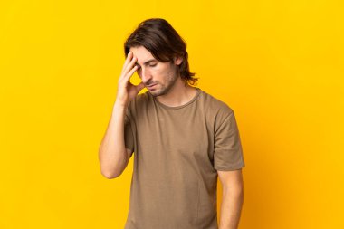 Sarı arka planda başağrısı olan yakışıklı genç bir adam.