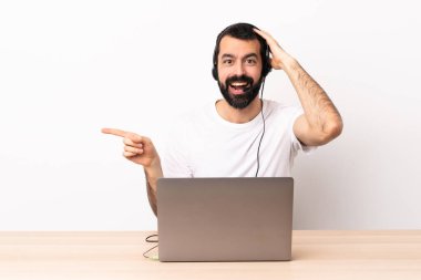 Tele-pazarlamacı beyaz bir adam kulaklıkla çalışıyor ve dizüstü bilgisayarı var. Şaşırmış ve işaret ediyor..