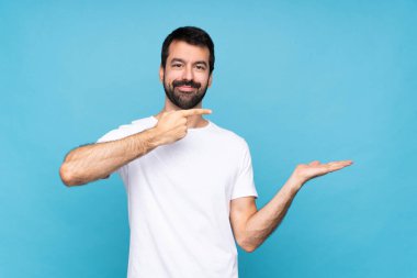 Mavi arka planda sakallı genç bir adam, bir ilan vermek için avucunda hayali bir şey tutuyor.