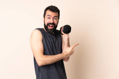 Beyaz sakallı sporcu halter kaldırıyor. Arka planda izole edilmiş ağırlık kaldırıyor. Şaşırmış ve işaret ediyor.