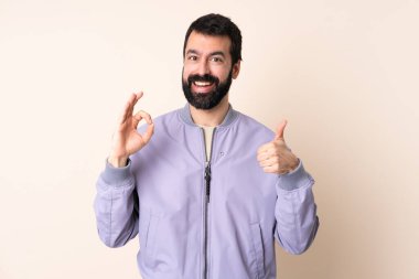 Sakallı beyaz bir adam izole edilmiş arka planda ceket giyiyor. Tamam işareti gösteriyor ve işaret veriyor.