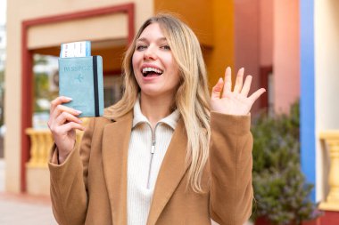 Genç, güzel, sarışın bir kadın, elinde pasaport, elinde mutlu bir ifadeyle selamlıyor.