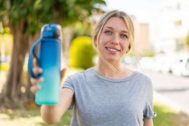 Açık havada genç sarışın bir kadın ve açık havada bir şişe su.